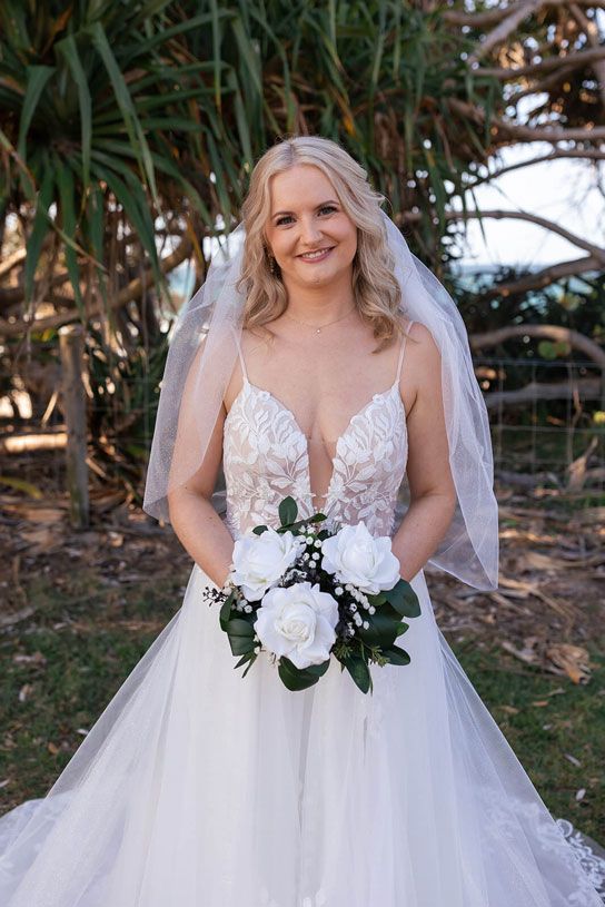 A bride in a wedding dress and veil is holding a bouquet of white roses.