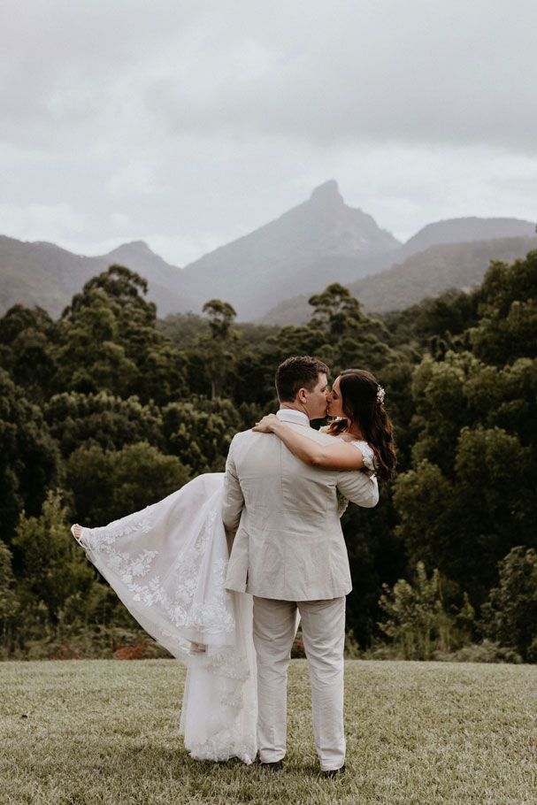 A bride and groom are kissing in front of a mountain.