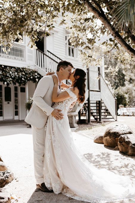 A bride and groom are kissing in front of a white building.