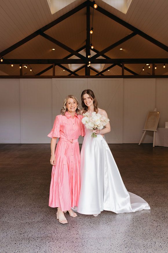 A bride and her mother are posing for a picture in a room.