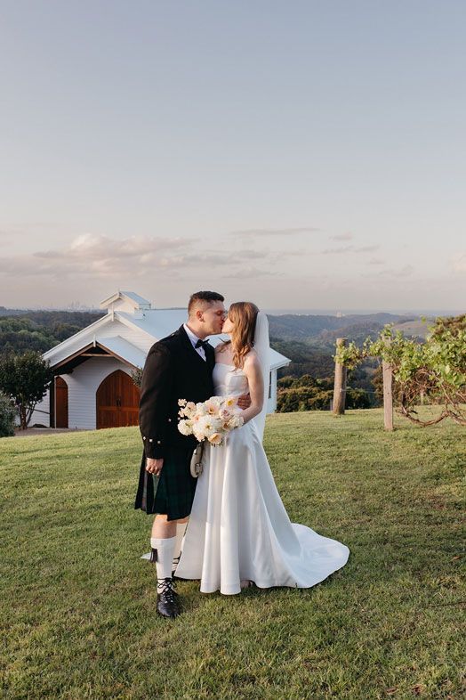 A bride and groom are kissing in front of a white building.