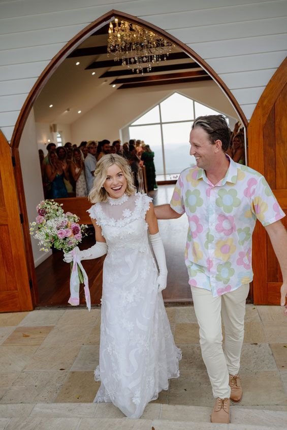 A bride and groom are walking out of a church holding hands.