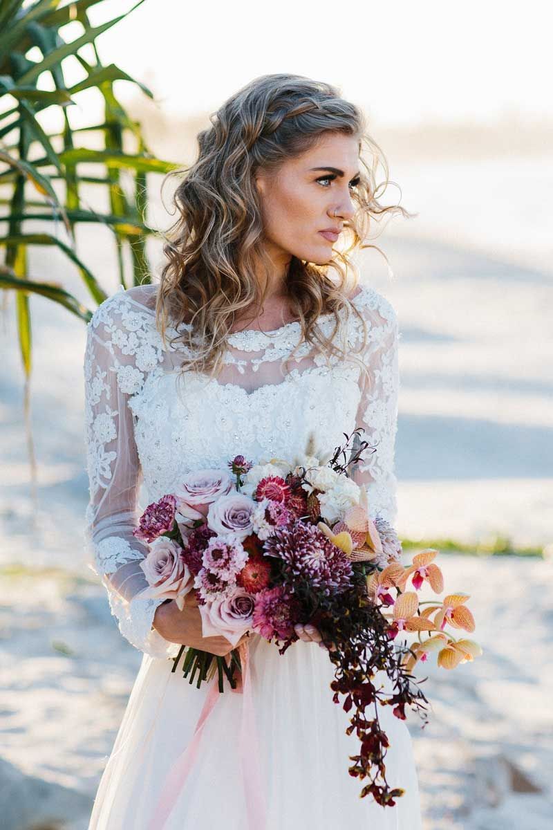 A bride in a white dress is holding a bouquet of flowers on the beach.