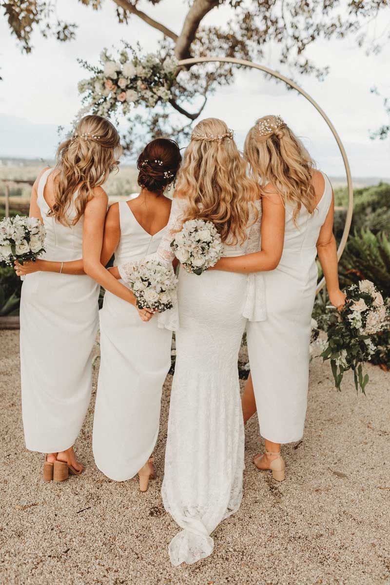 A bride and her bridesmaids are standing next to each other in front of a tree.