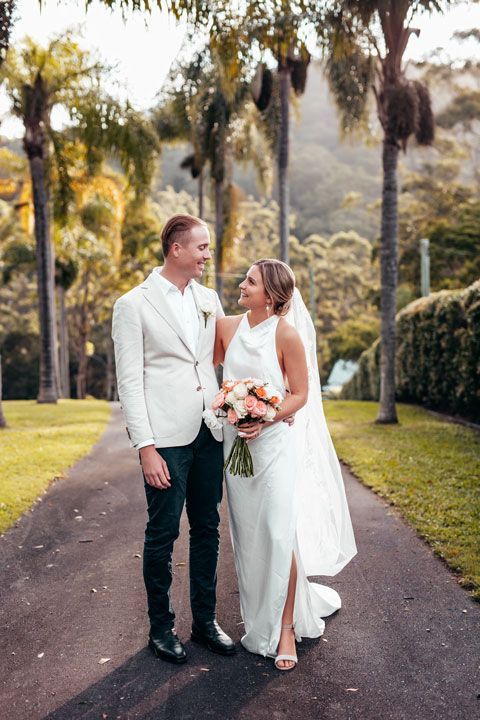 A bride and groom are standing next to each other on a path.