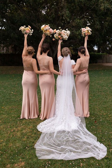 A bride and her bridesmaids are holding up their bouquets in the air.