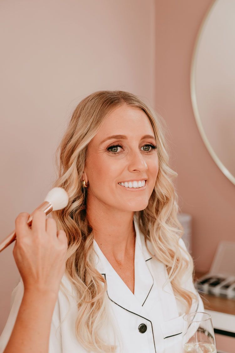 A woman is smiling while getting her makeup done in front of a mirror.
