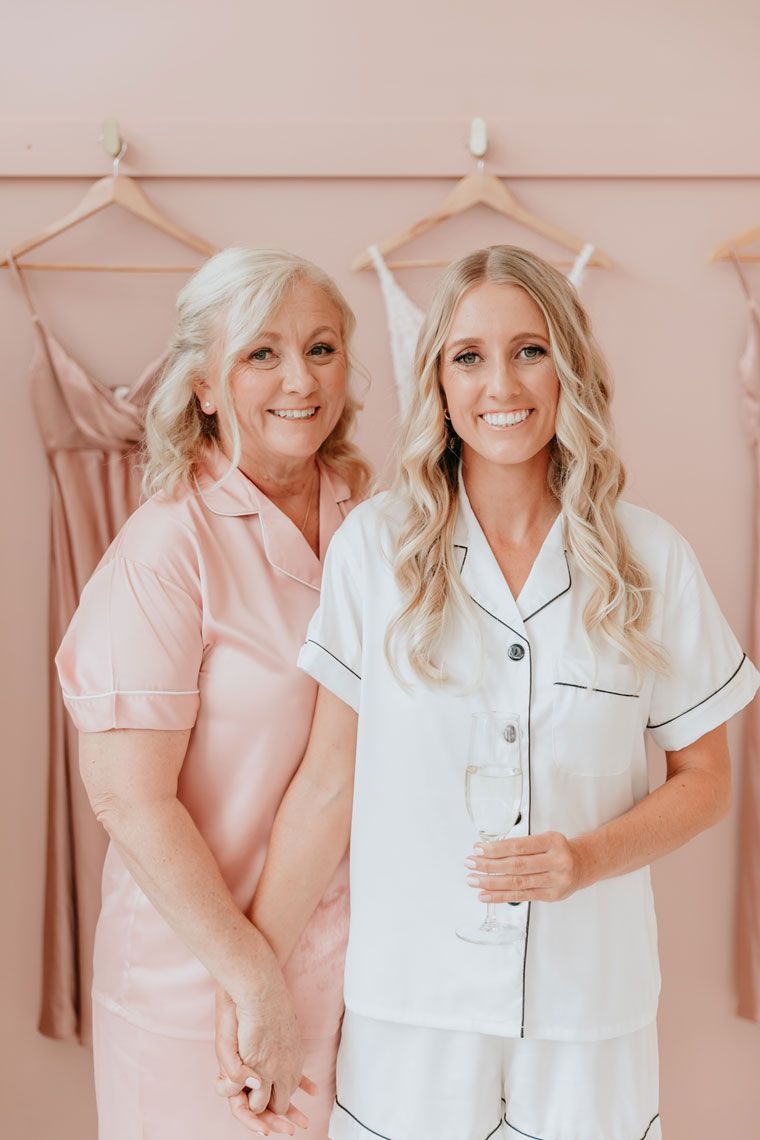 Two women are standing next to each other in front of a pink wall holding hands.