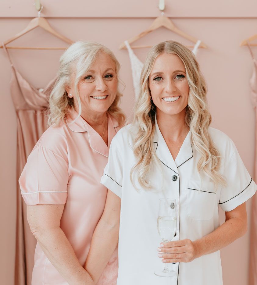Two women are standing next to each other in front of a pink wall.