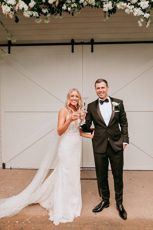 A bride and groom are standing next to each other holding glasses of champagne.