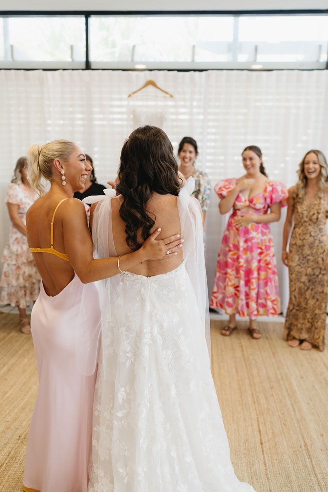 A bride and her bridesmaids are hugging each other in a room.