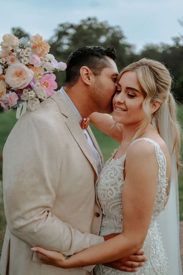 A bride and groom are kissing in front of a bouquet of flowers.