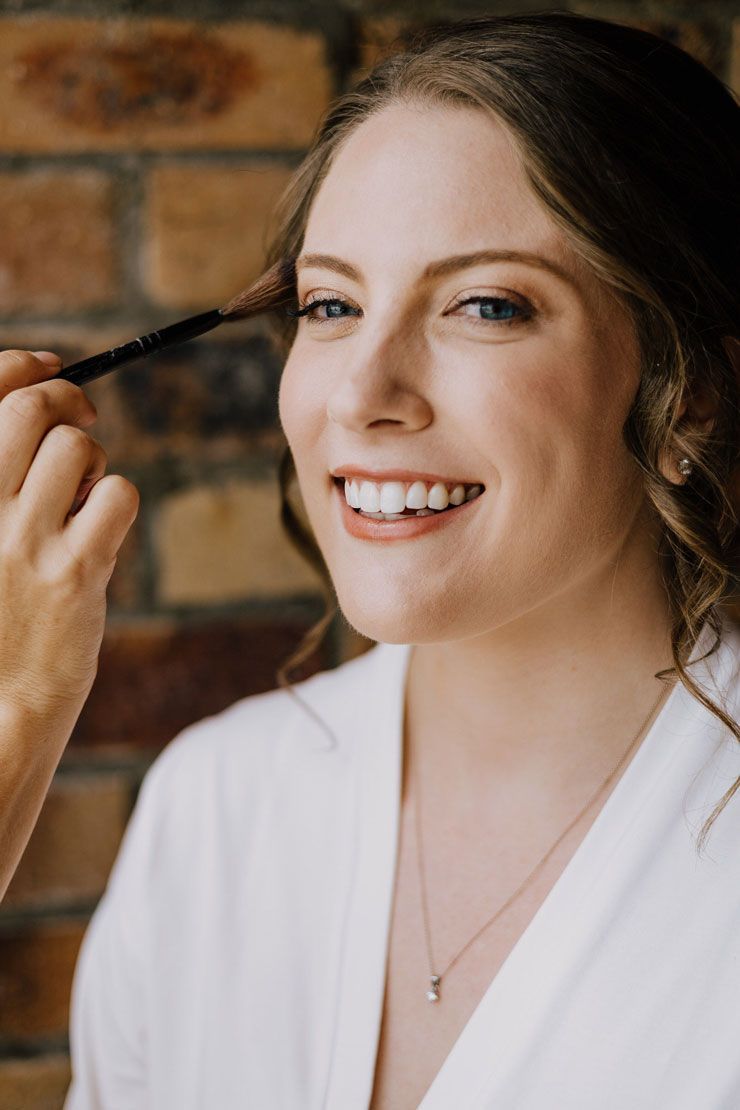 A woman is smiling while getting her makeup done by a makeup artist.