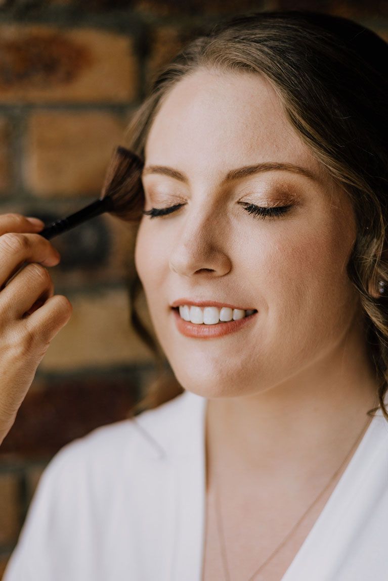 A woman is applying makeup to her face with a brush.