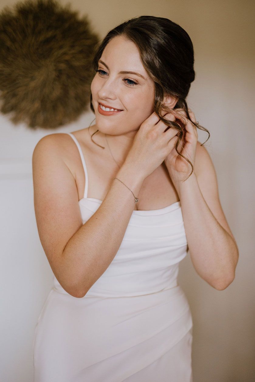 A woman in a white dress is putting on her earrings.