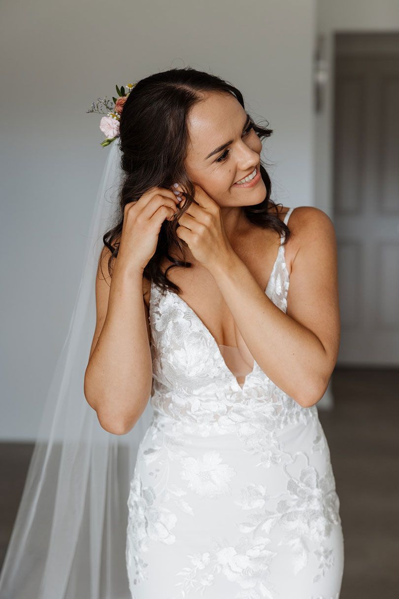 A bride in a wedding dress is putting on her earrings.