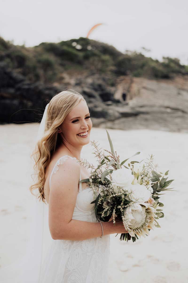 A bride in a white dress is holding a bouquet of flowers on the beach.