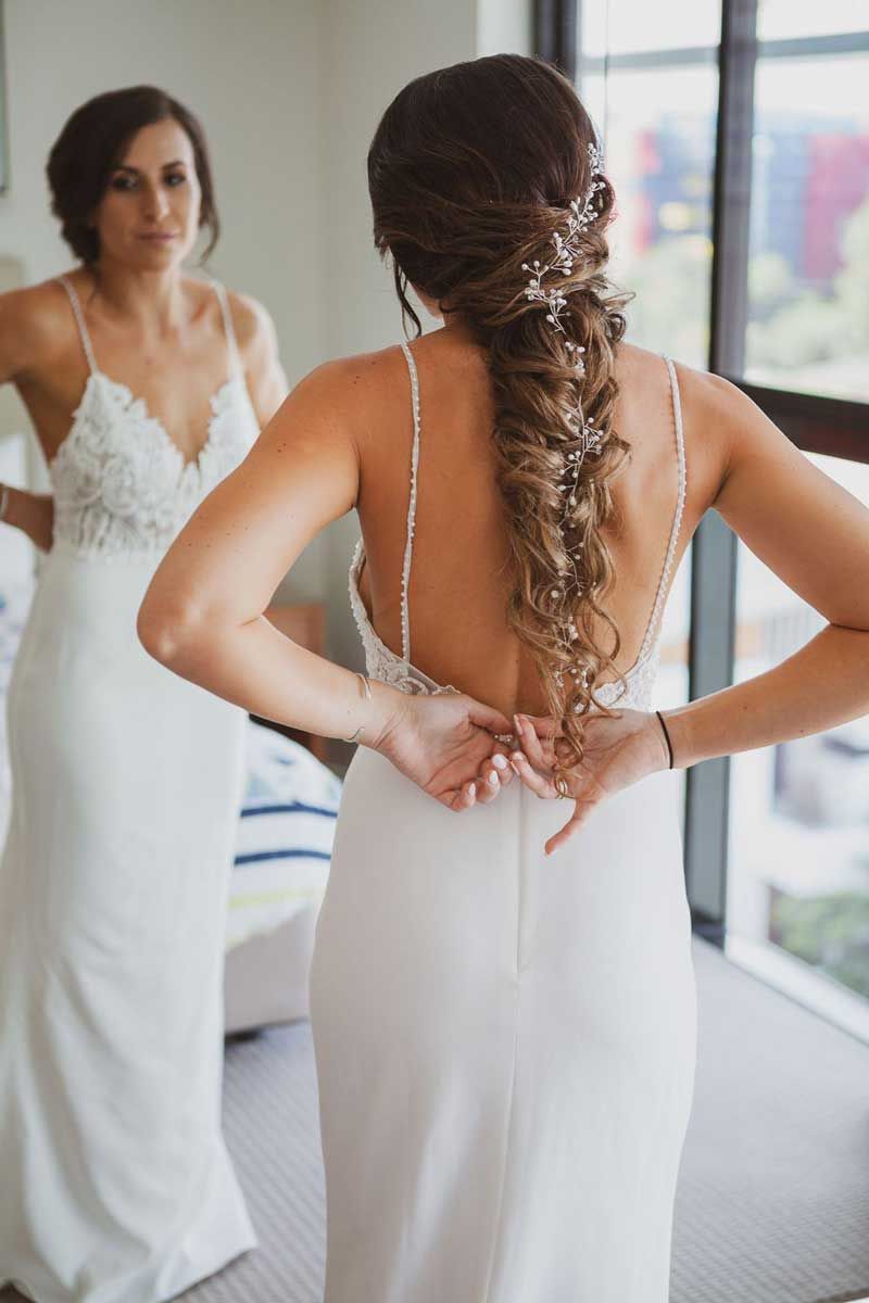 A bride is putting on her wedding dress in front of a mirror.