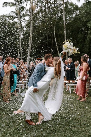 A bride and groom are kissing in front of their wedding guests.