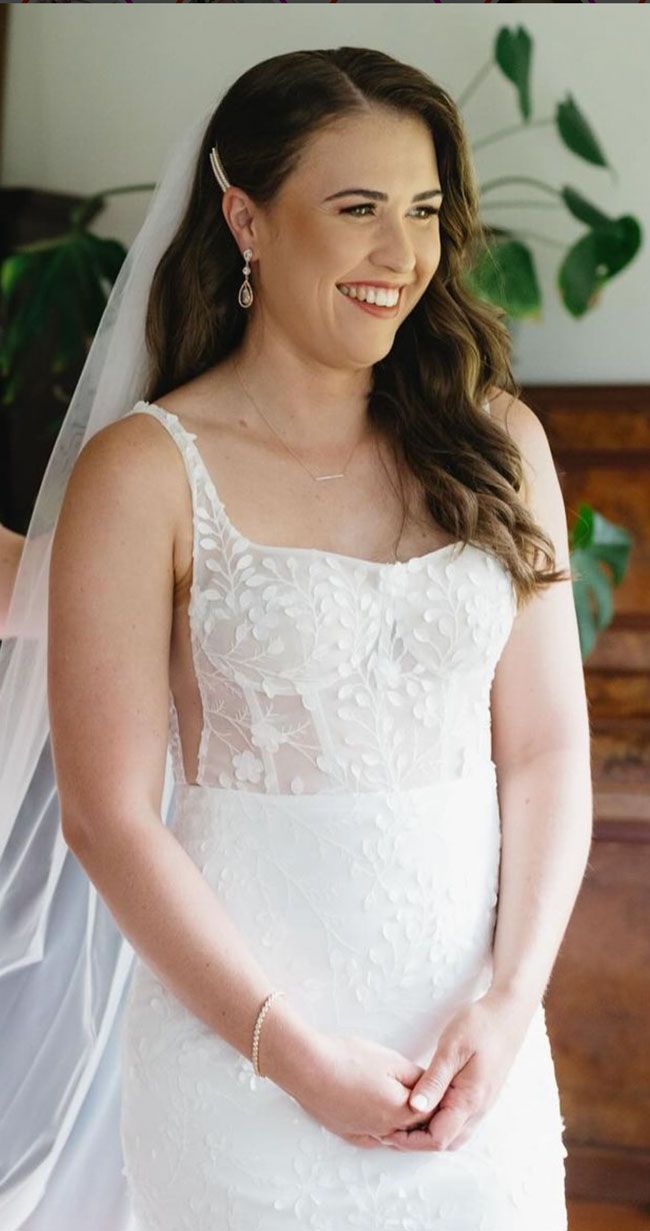 A woman in a white wedding dress and veil is smiling.