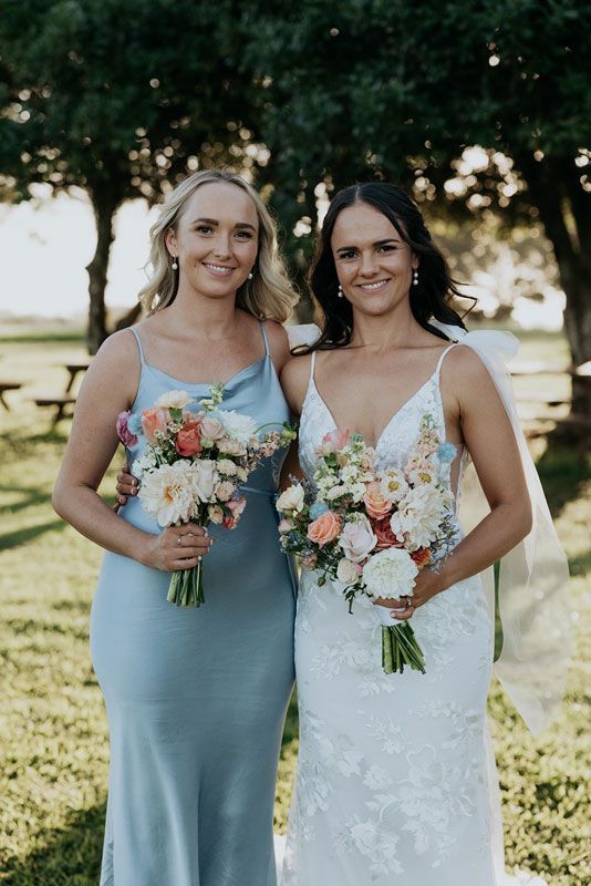 A bride and her bridesmaid are posing for a picture while holding bouquets of flowers.