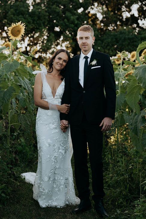 A bride and groom are posing for a picture in a field of sunflowers.