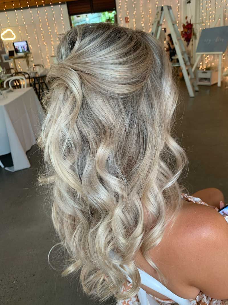 A woman with blonde hair is sitting in a chair with her hair in a half up half down hairstyle.