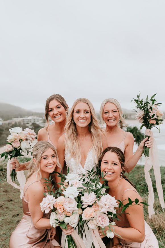 A bride and her bridesmaids are posing for a picture on top of a hill.