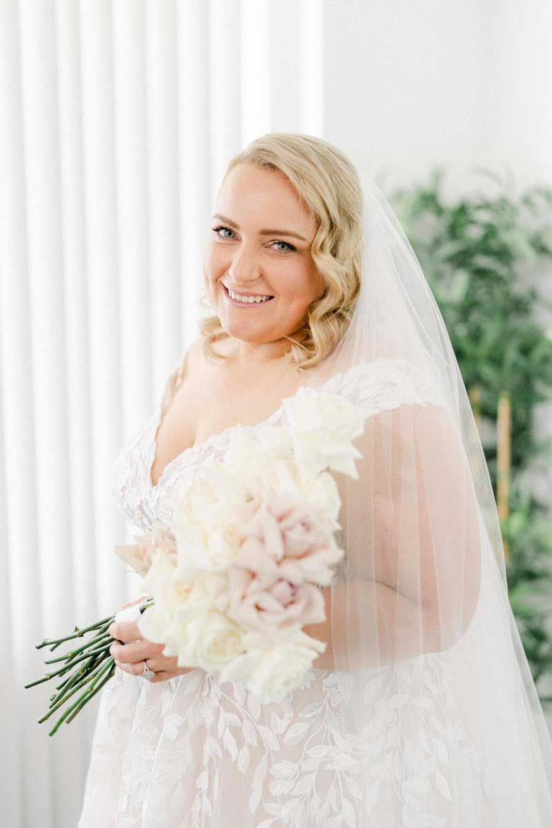 The bride is wearing a veil and holding a bouquet of white flowers.
