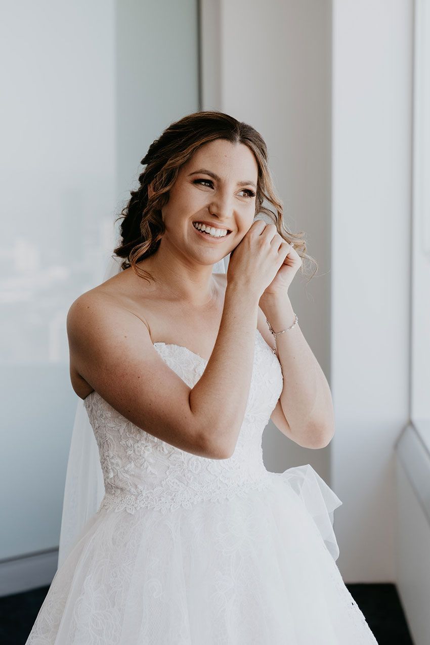 A bride in a wedding dress is standing in front of a window.