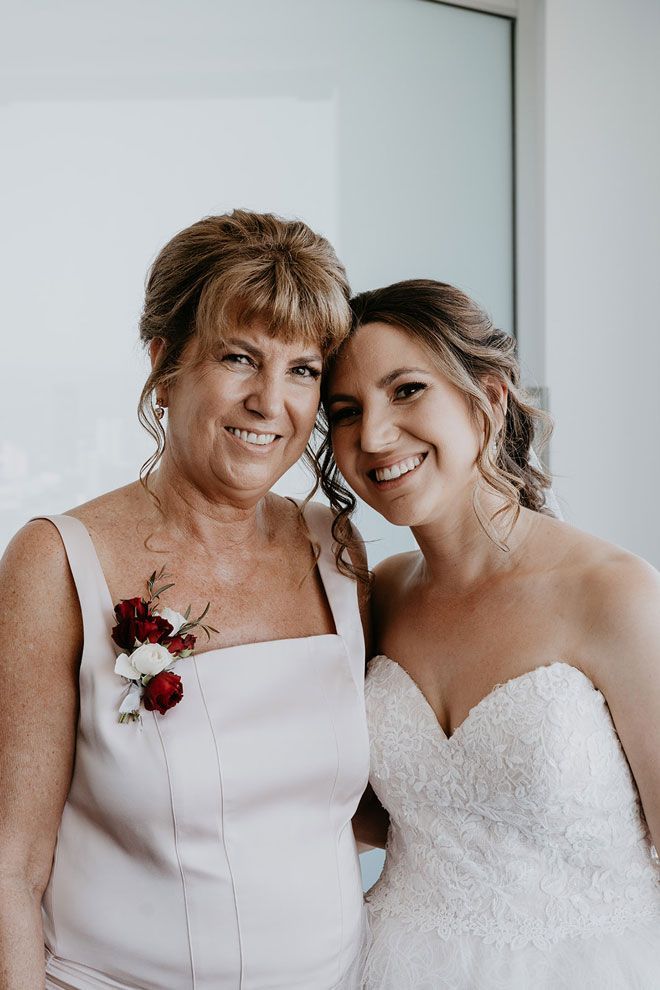 A bride and her mother are posing for a picture together.