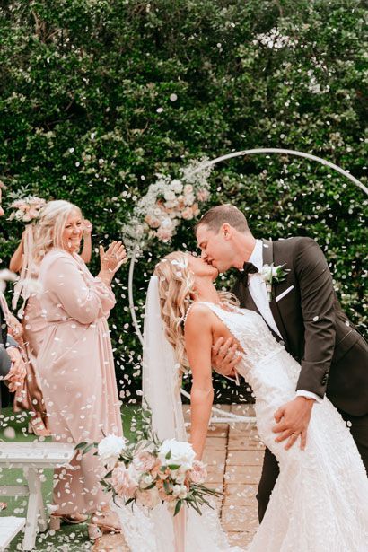 A bride and groom are kissing at their wedding ceremony while confetti is being thrown at them.