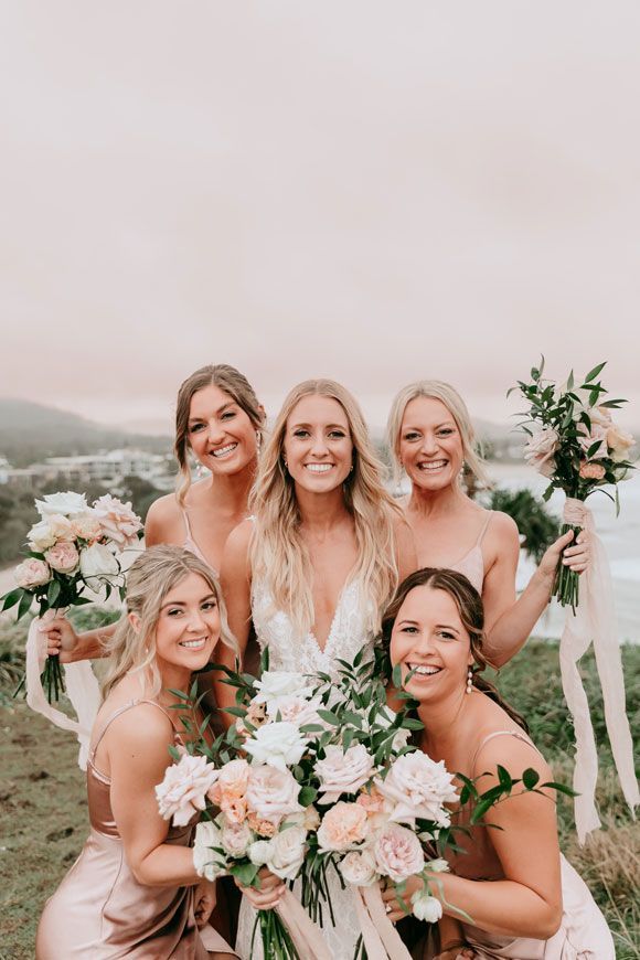 A bride and her bridesmaids are posing for a picture while holding bouquets of flowers.