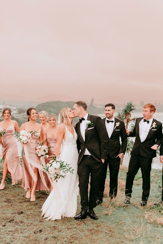 A bride and groom are kissing in front of their wedding party.