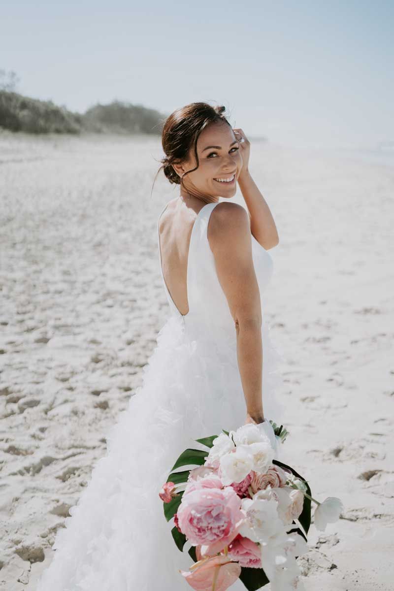 A bride in a white dress is holding a bouquet of flowers on the beach.