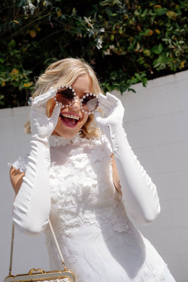 A woman in a white dress and long white gloves is wearing sunglasses.