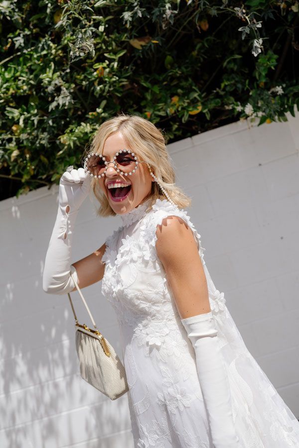 A woman in a white dress and white gloves is laughing.