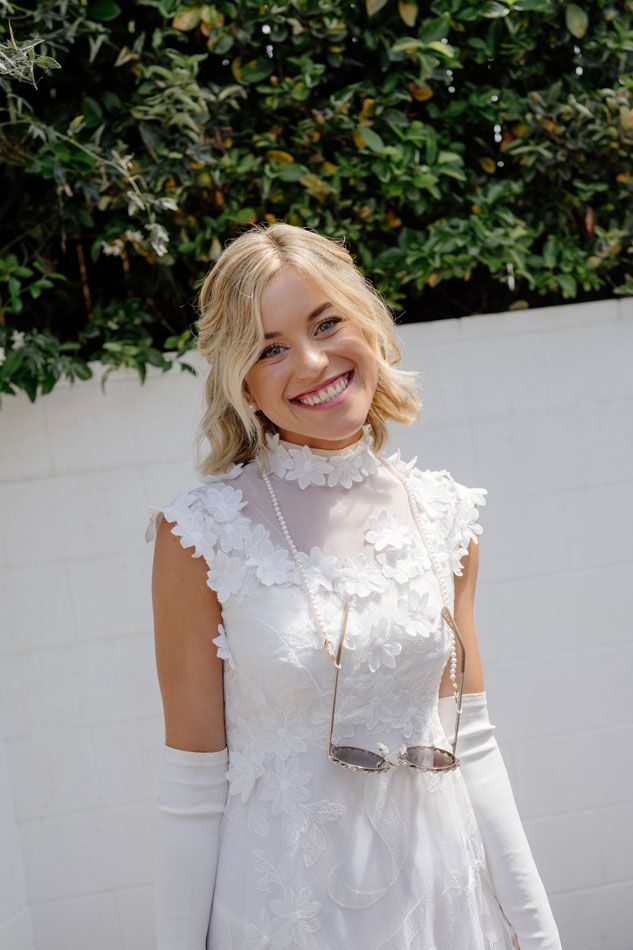 A woman in a white dress and white gloves is smiling.