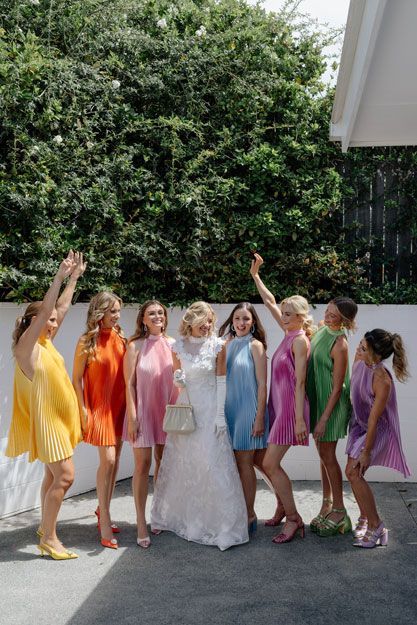 A bride and her bridesmaids are posing for a picture in colorful dresses.