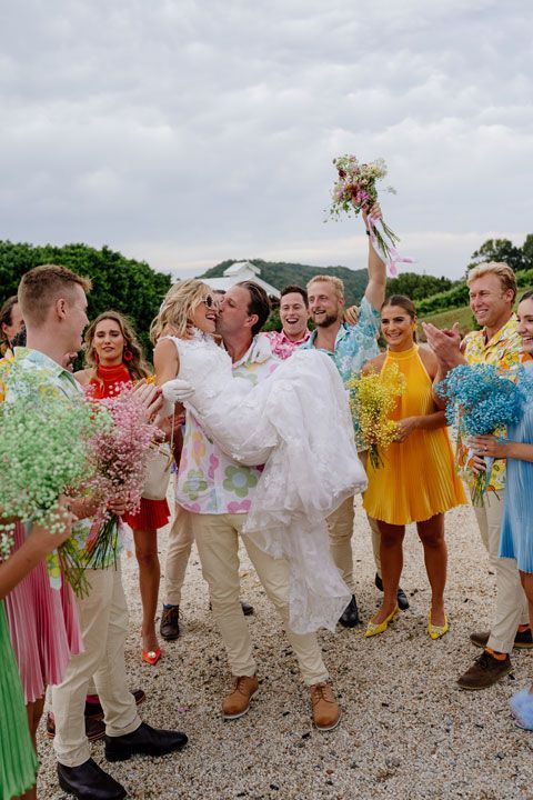 A bride and groom are kissing in front of their wedding party.