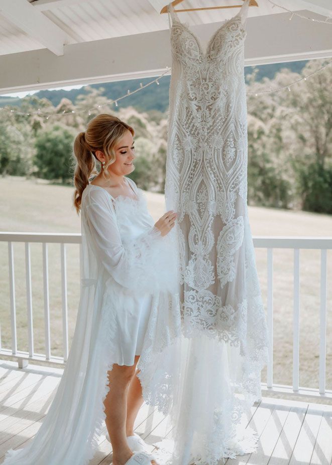 A woman in a white robe is holding a wedding dress hanging on a railing.