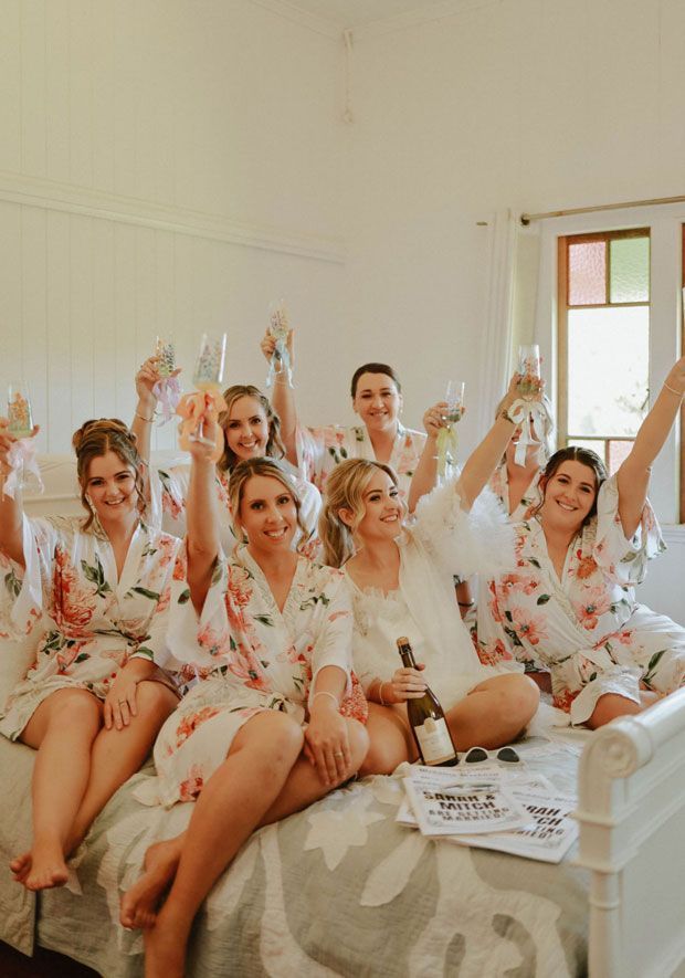 A group of women are sitting on a bed toasting with champagne.