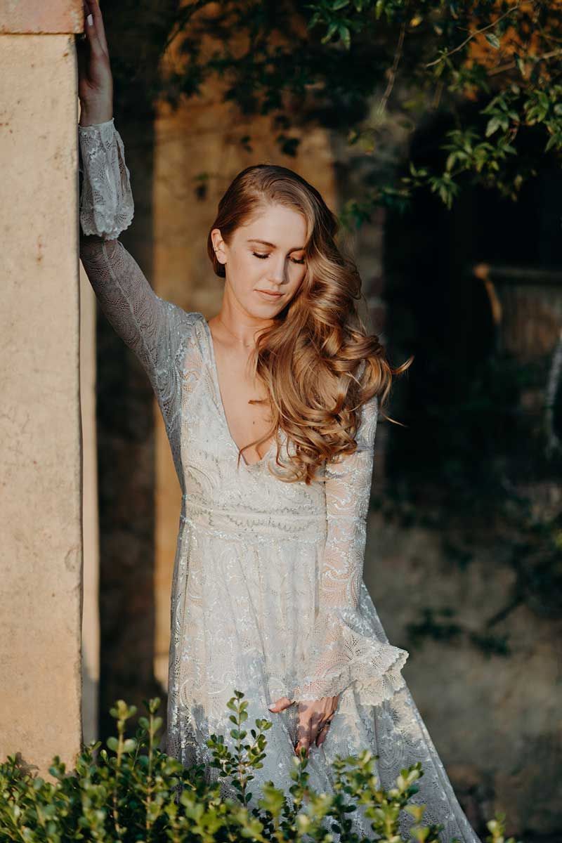 A woman in a white dress is leaning against a wall.