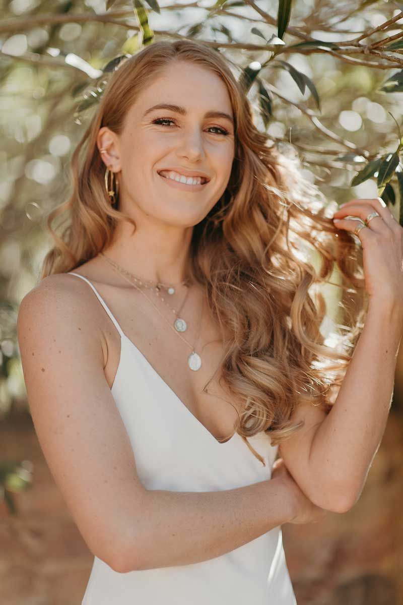 A woman in a white dress is smiling and holding her hair.