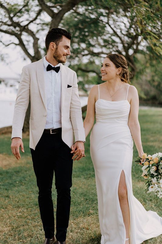 A bride and groom are holding hands while walking in a field.