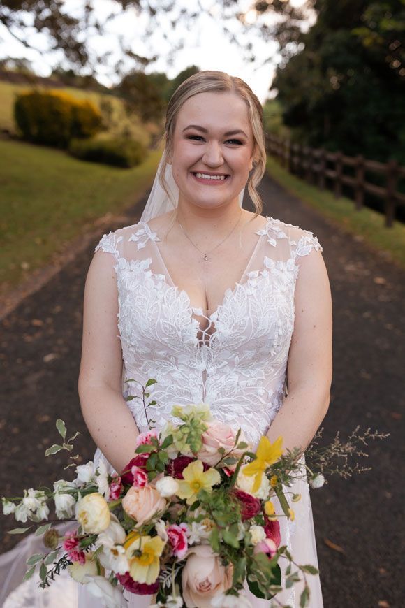 A bride in a wedding dress is holding a bouquet of flowers and smiling.