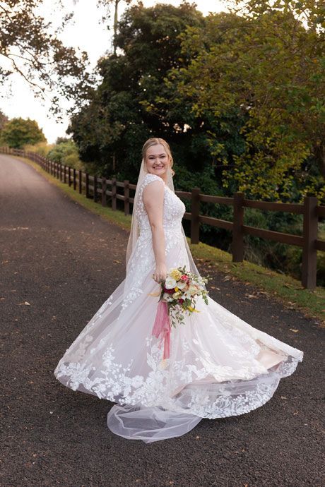 A bride in a wedding dress is standing on a road holding a bouquet of flowers.