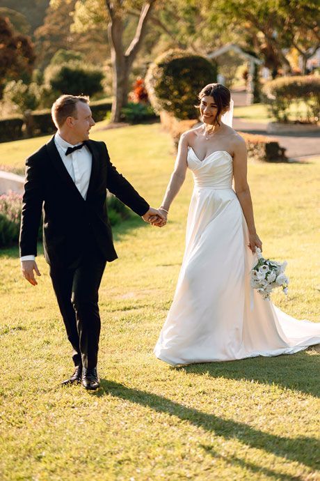 A bride and groom are walking in the grass holding hands.