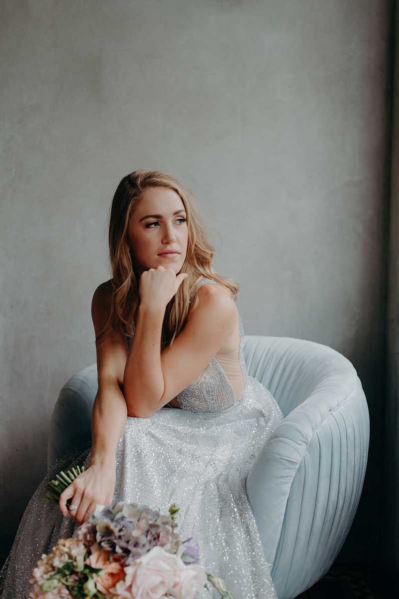 A woman in a wedding dress is sitting in a chair holding a bouquet of flowers.