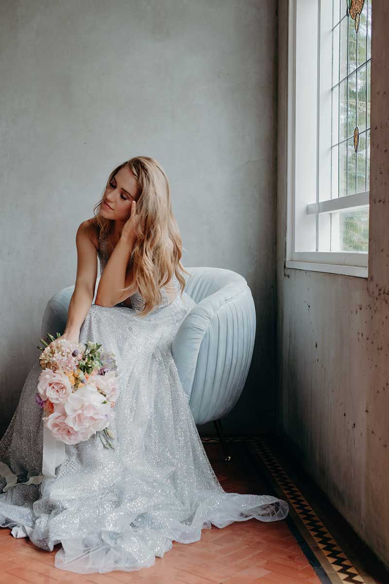 A woman in a wedding dress is sitting in a chair holding a bouquet of flowers.
